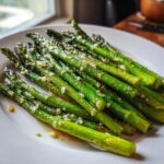 A close-up of bright green roasted asparagus spears seasoned with minced garlic and oil, served on a white plate.