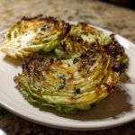 Three beautifully roasted cabbage steaks seasoned with herbs, showing caramelized edges on a light plate.