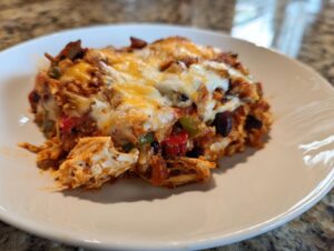 A close-up serving of cheesy fajita chicken casserole with shredded chicken, peppers, and black beans on a white plate.