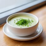 A white bowl filled with silky smooth leek soup, garnished generously with fresh chopped chives.