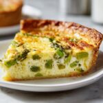 Close-up of a thick slice of asparagus quiche showing bright green asparagus pieces in a creamy egg filling.
