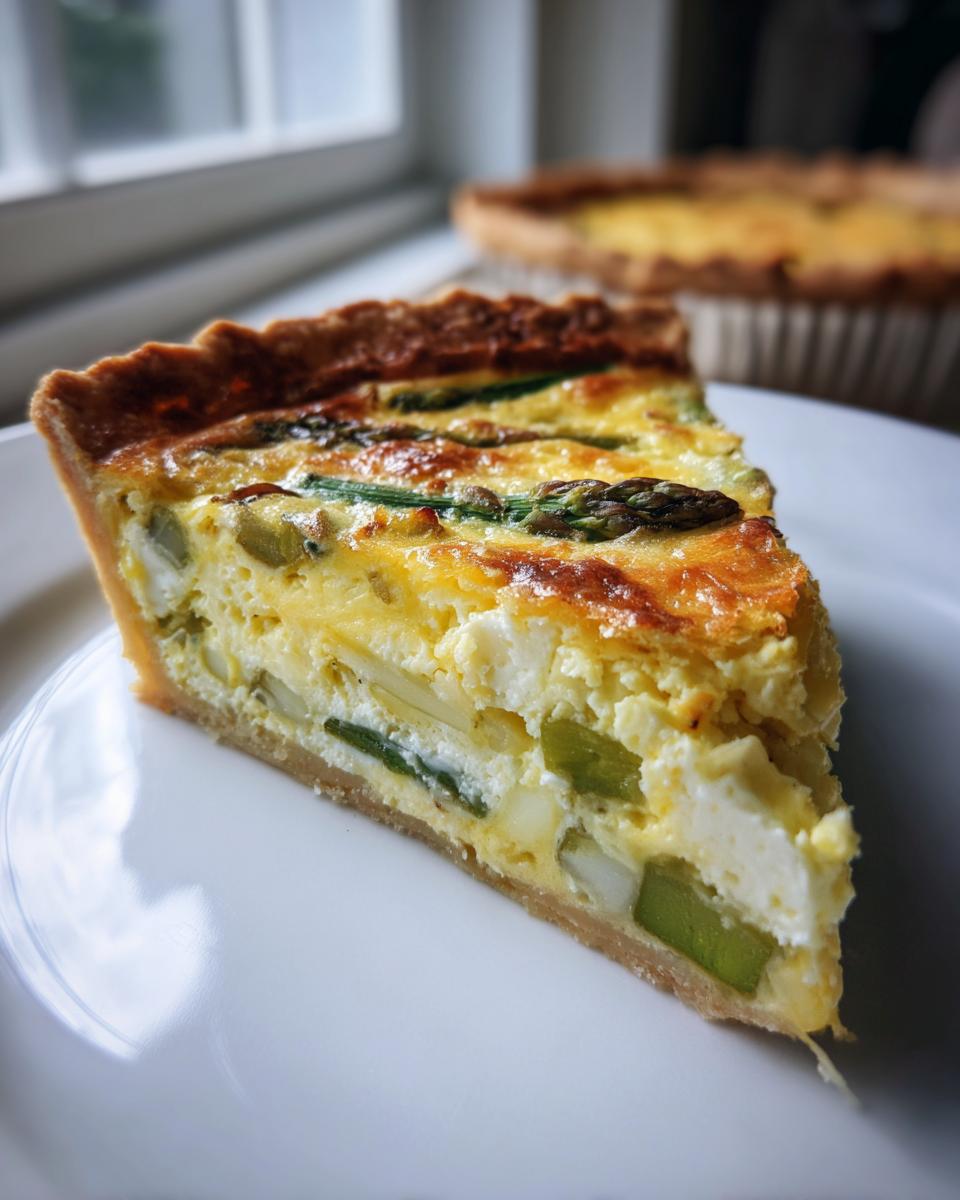 A close-up of a perfect slice of Asparagus quiche showing the flaky crust and creamy filling with green asparagus pieces.