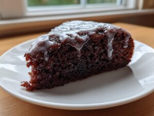 A close-up of a rich, dark slice of dr pepper cake topped with a thin white glaze.