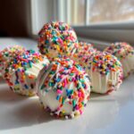 Close-up of several white chocolate-coated starbucks cake pop treats covered in bright rainbow sprinkles.