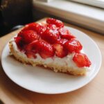 A close-up slice of strawberry pizza featuring a shortbread crust, thick cream layer, and glossy fresh strawberries.