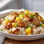 A close-up of a bowl filled with sweet and savory pineapple chicken and rice, garnished with green onions.
