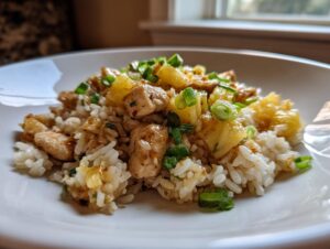 Close-up of a plate featuring sweet and savory pineapple chicken and rice topped with green onions.