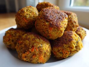 A close-up stack of golden brown vegetarian lentil meatballs with visible quinoa and carrot pieces.