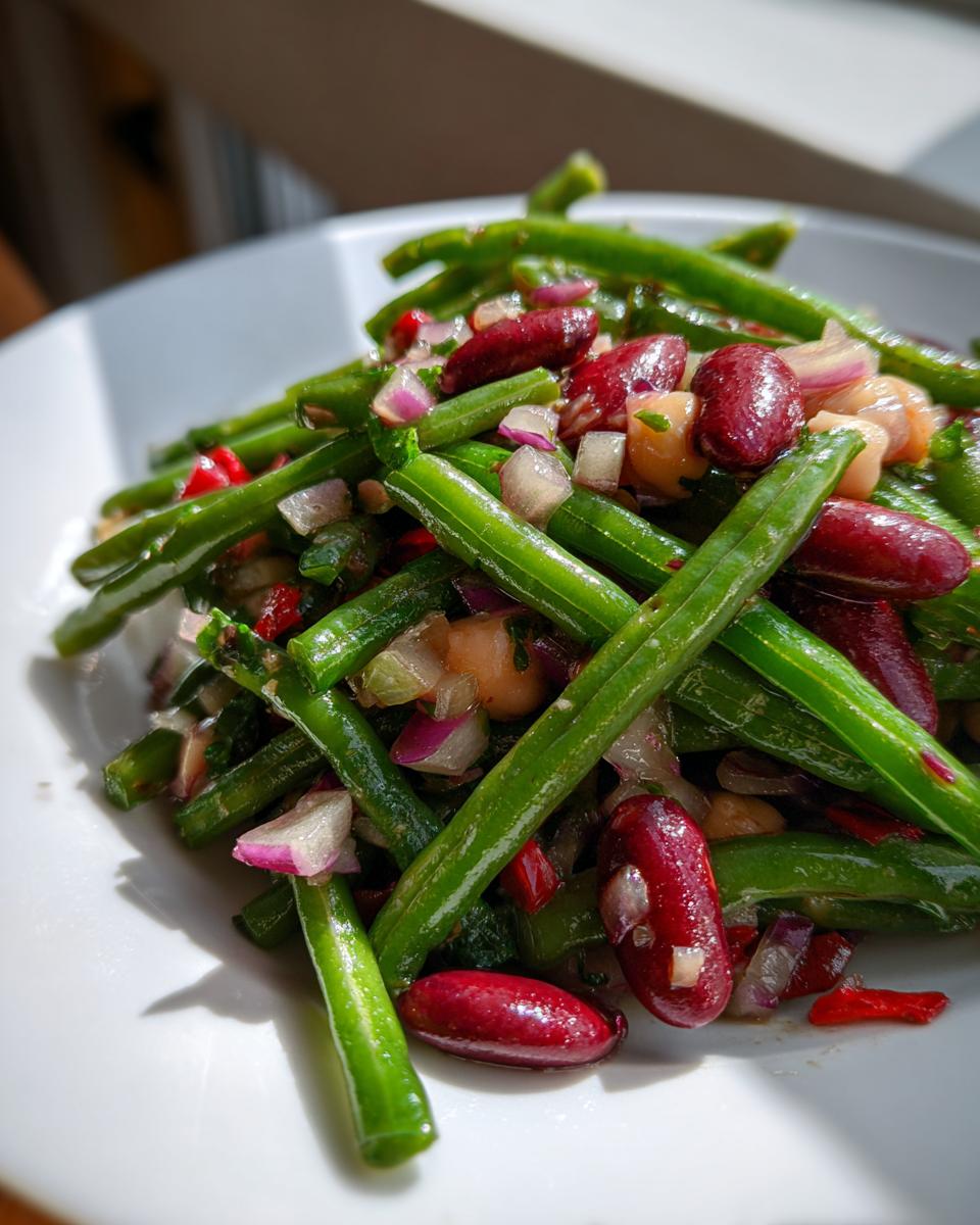 A close-up of a vibrant three bean salad featuring bright green beans, dark red kidney beans, and diced red onion.