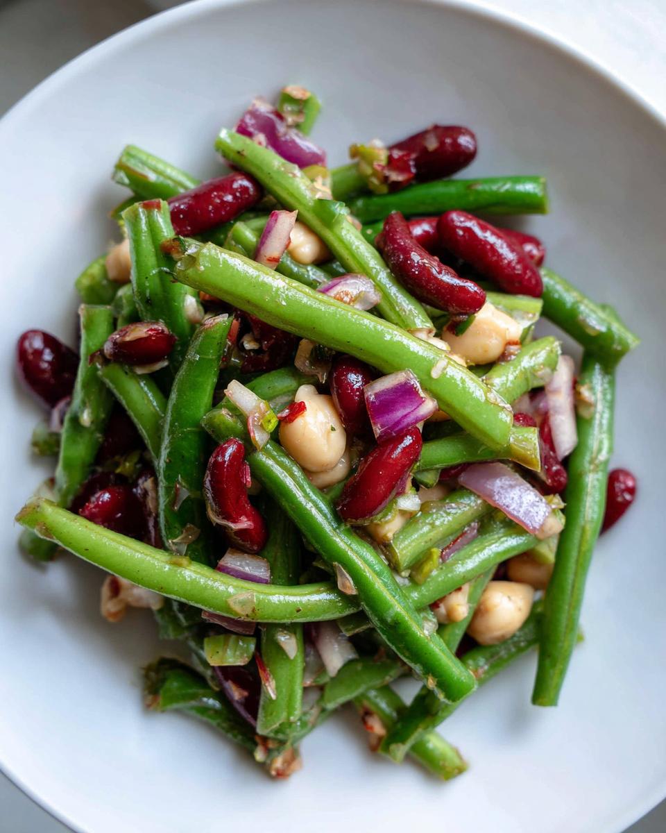 Close-up overhead view of a vibrant three bean salad featuring green beans, kidney beans, chickpeas, and red onion.