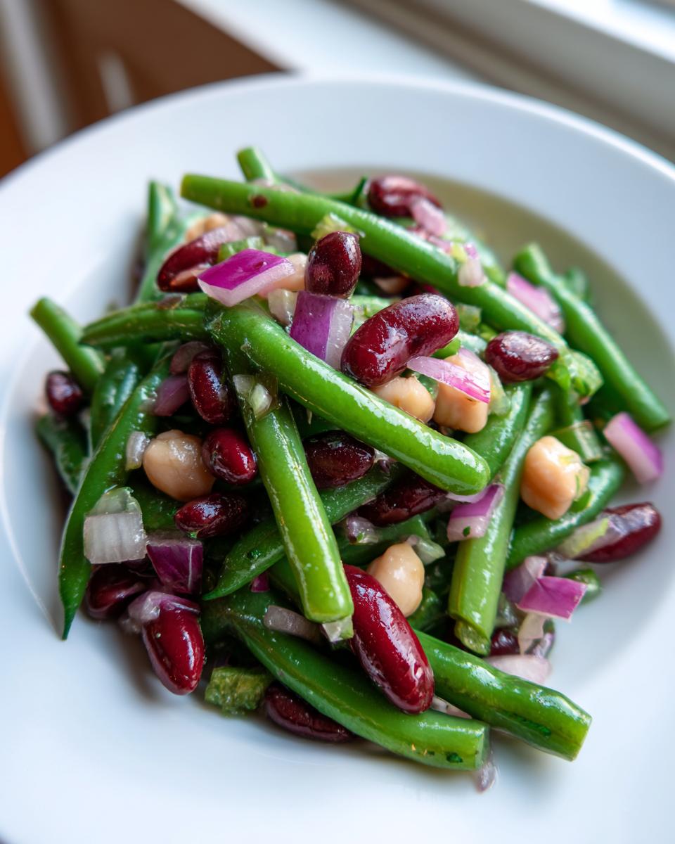 Close-up of a vibrant three bean salad featuring bright green beans, dark red kidney beans, chickpeas, and diced red onion.