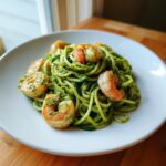Close-up of zucchini noodles pesto shrimp tossed in vibrant green pesto sauce on a white plate.
