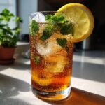 A tall glass filled with bubbling Mint Iced Tea, ice cubes, fresh mint leaves, and a lemon slice garnish.