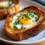 Close-up of a golden-brown Egg in a Hole topped with fresh green chives and cracked pepper.