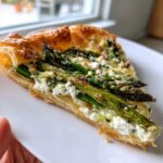 Close-up of a slice of Asparagus goat cheese tart featuring flaky pastry, roasted asparagus spears, and creamy goat cheese.