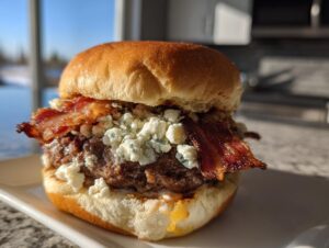 A close-up of a juicy Bacon Blue Cheese Burger topped with crumbled blue cheese and crispy bacon strips on a brioche bun.