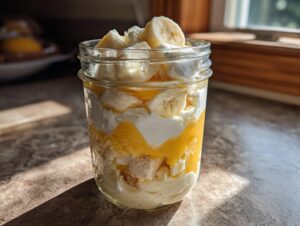 Close-up of a layered banana pudding parfait in a mason jar with fresh banana slices on top.