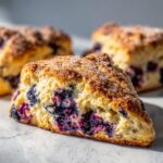 A close-up, cross-section view of a freshly baked Blueberry cream scone, studded with juicy blueberries and topped with coarse sugar.