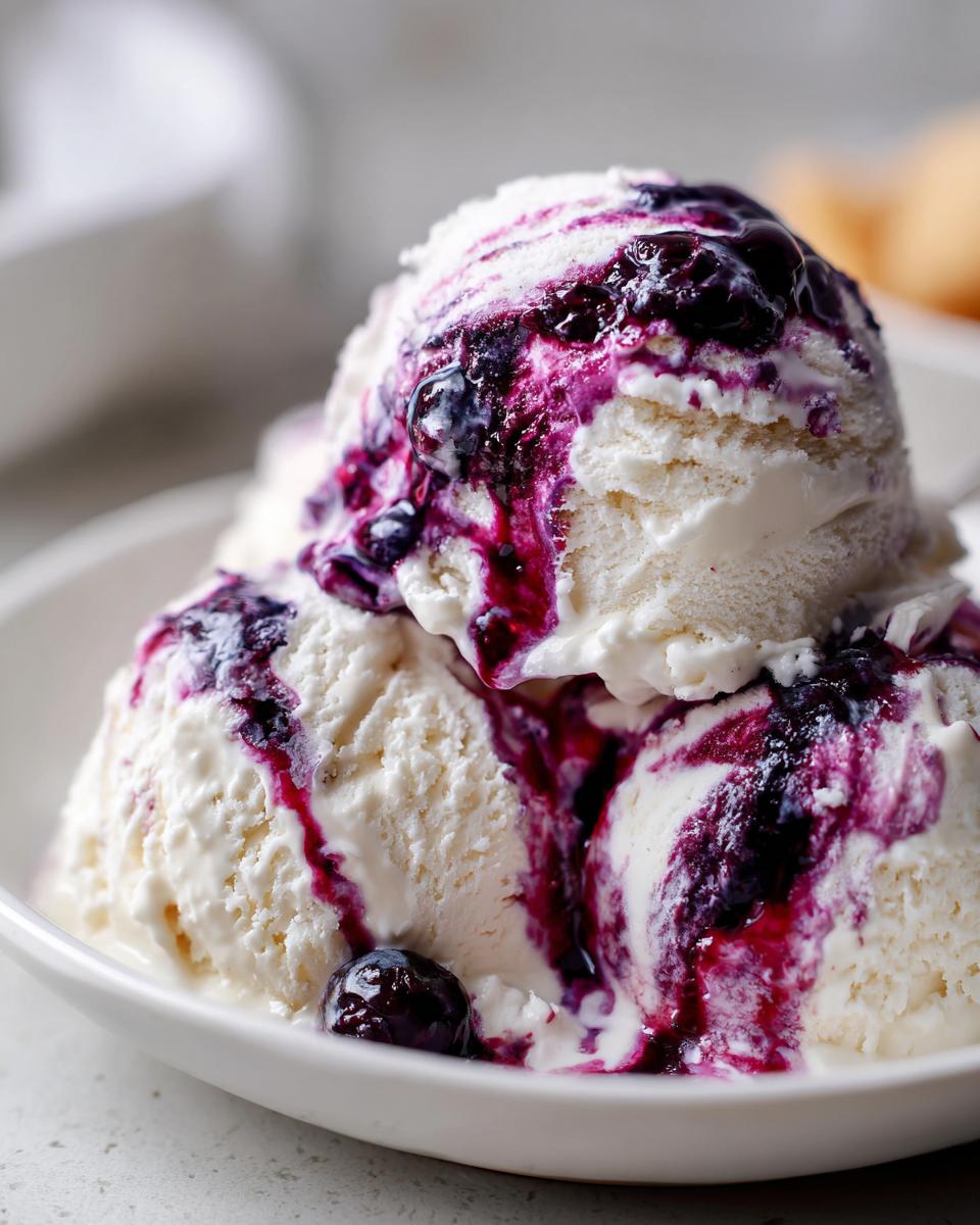 Three scoops of vanilla Blueberry swirl ice cream drizzled generously with rich, dark blueberry sauce in a white bowl.