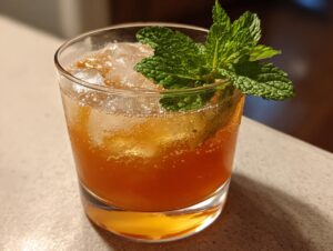Close-up of a Bourbon peach smash cocktail served over ice in a rocks glass, garnished with fresh mint.