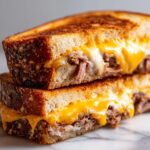 Close-up of a stacked Brisket grilled cheese sandwich halves showing gooey melted cheddar and white cheese oozing out.