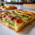 Close-up of a golden, flaky slice of Cheesy asparagus tart topped with bright green asparagus spears.