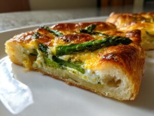 Close-up of a thick slice of cheesy asparagus tart showing a fluffy crust and bright green asparagus spears.