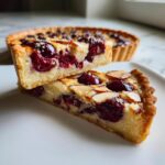 Two stacked slices of a homemade Cherry almond tart showing the thick almond filling and bright red cherries.