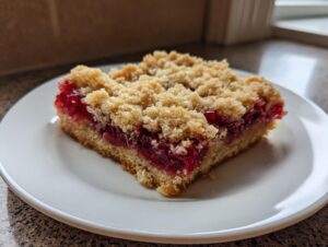 A square slice of Cherry Cobbler Bars featuring a thick layer of bright red cherry filling topped with a golden crumble.