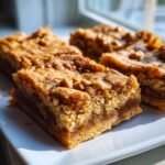 Four rich, golden-brown squares of chewy butterscotch blondies with visible butterscotch chips, resting on a white plate.