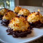 Close-up of several golden-brown chocolate dipped macaroon treats arranged on a white plate.