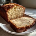 A loaf of moist Cinnamon applesauce bread, partially sliced, showing the soft interior speckled with cinnamon.