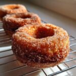 Close-up of a freshly baked, golden brown applesauce donuts coated in cinnamon sugar, resting on a wire cooling rack.
