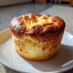 A tall, golden-brown Classic Cheese Soufflé served individually on a white plate, showing its impressive rise.