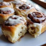 Close-up of a freshly baked Classic cinnamon roll, broken open to show the soft interior and dripping with white cream cheese icing.