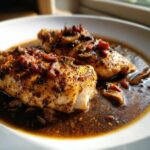 Two pieces of perfectly cooked chicken served in a rich, dark sauce with mushrooms and bacon, representing Classic coq au vin.
