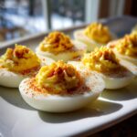Close-up of several Classic deviled egg halves filled with piped yolk mixture and sprinkled with paprika.