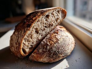 A rustic loaf of cocoa nib sourdough bread, sliced open to show the open, airy crumb texture with visible cocoa nibs.