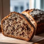 Close-up of a thick slice of cocoa nib sourdough bread showing the airy crumb studded with dark cocoa nibs.