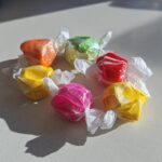 Six colorful pieces of homemade salt water taffy, individually wrapped in twisted wax paper, arranged in a circle.
