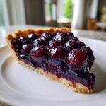 A close-up of a slice of Concord grape tart showing a buttery crust filled with glossy, deep purple Concord grapes.