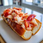 A close-up of a Connecticut warm butter lobster roll overflowing with bright red and white lobster meat in a toasted split-top bun.
