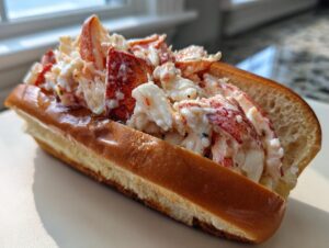 A close-up of a Connecticut warm butter lobster roll overflowing with chunks of lobster meat in a buttered, toasted split-top bun.
