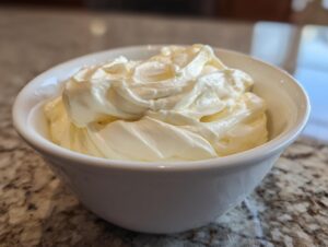 A close-up of creamy, swirled Cottage cheese vanilla mousse served in a small white bowl on a granite countertop.