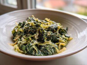 A close-up of a serving of creamy Cabbage alfredo, featuring shredded green cabbage coated in a rich white sauce, in a white bowl.