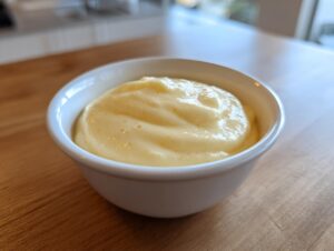 A close-up of thick, creamy homemade vanilla pudding served in a small white bowl on a wooden surface.
