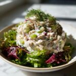 A scoop of creamy Rotisserie chicken salad mixed with celery and red onion, topped with fresh dill, served over mixed lettuce.