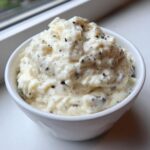 A close-up of creamy vanilla bean rice pudding speckled with dark vanilla seeds, served in a white bowl.