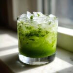 A vibrant green Cucumber Mint Cooler drink filled with crushed ice and mint leaves.