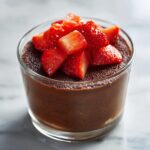 A glass serving of rich dark chocolate mousse topped with fresh, sliced strawberries.